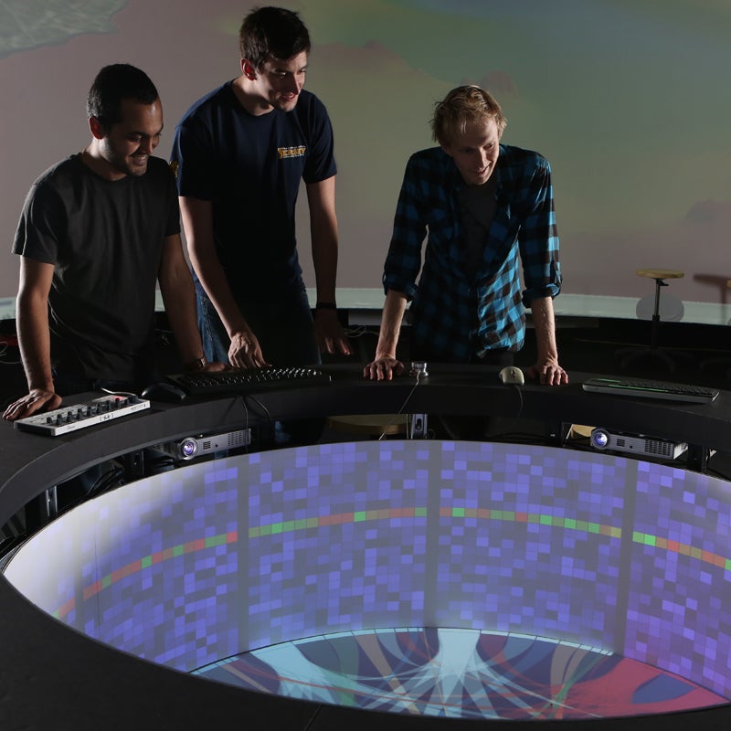 Three people looking down on a 360 degree monitor