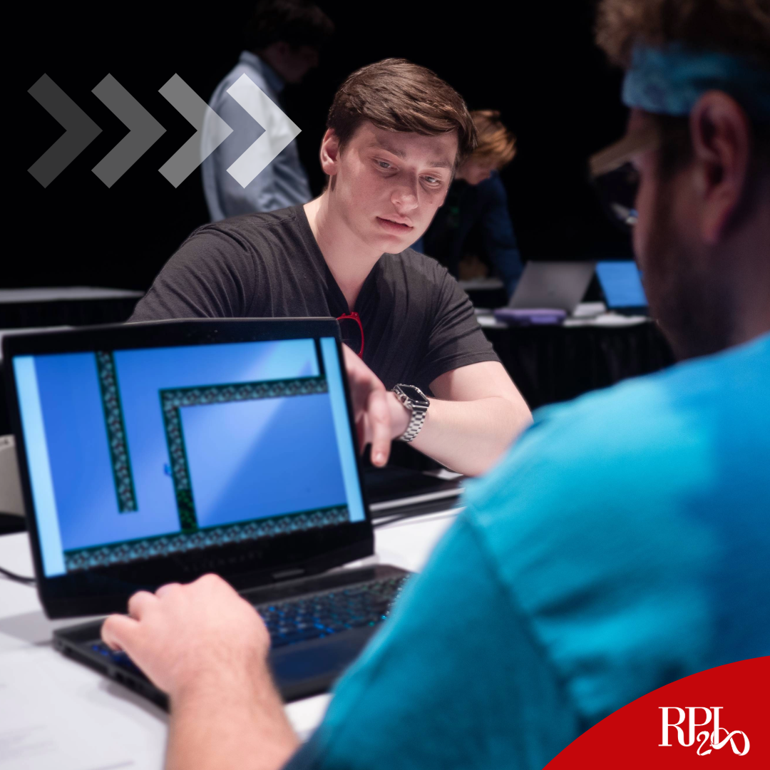 a male student explaining his game to a player wearing a blue shirt using a laptop