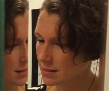 a caucasian woman with brown hair, seemingly, looking at her reflection